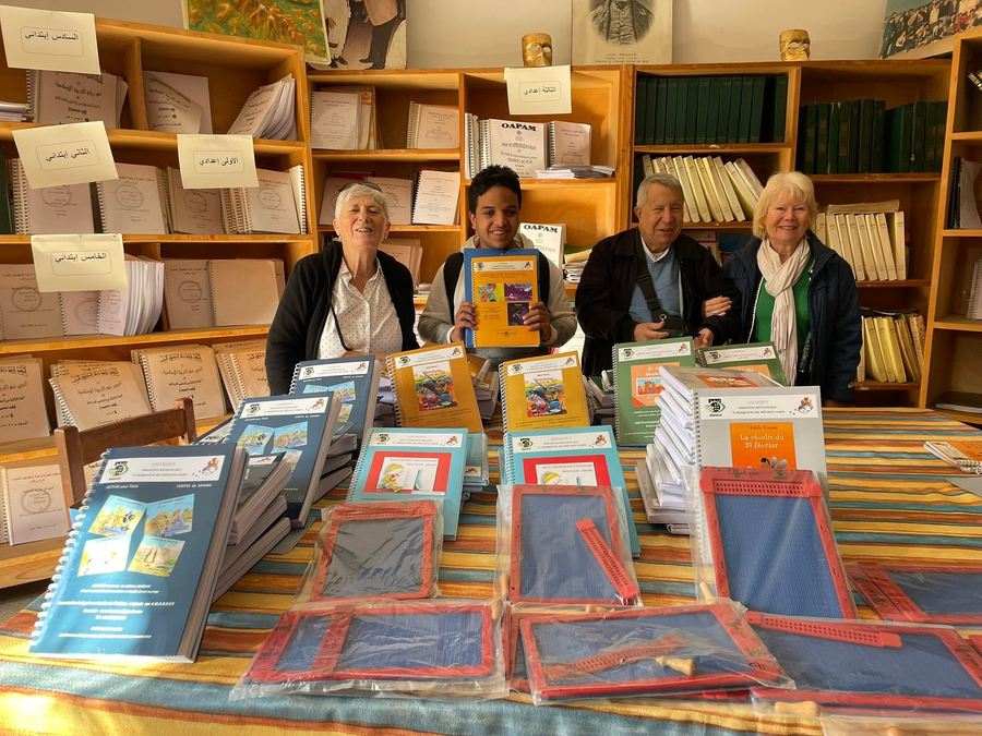 Une équipe d'AMARDEV pose avec le personnel éducatif d'une école, entourée de piles de livres en braille et de tablettes de lecture, dans une bibliothèque scolaire