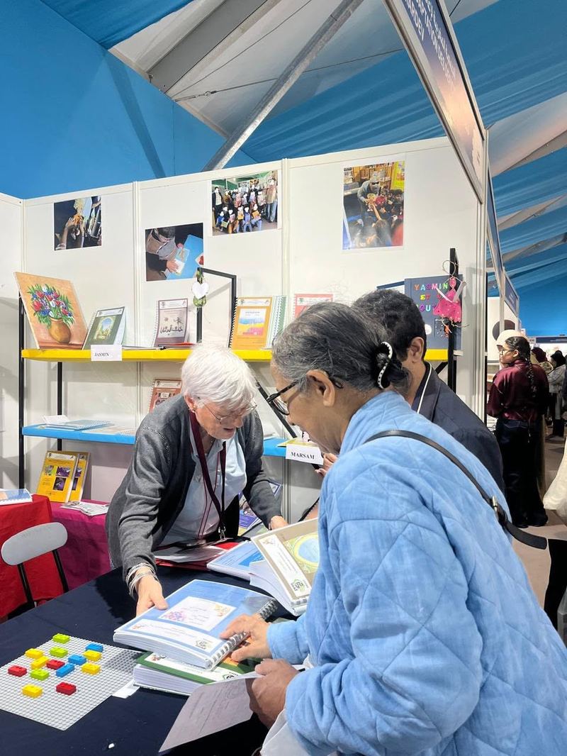 Deux bénévoles examinent ensemble des livrets et des briques braille sur la table du stand