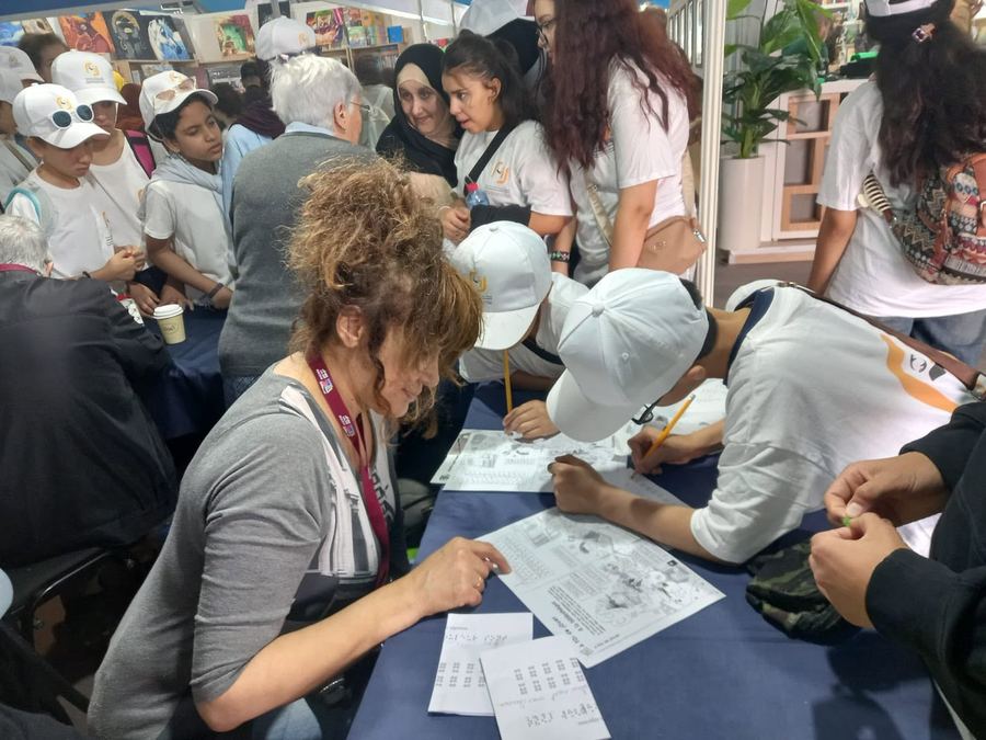 Une bénévole AMARDEV explique une planche en braille à un groupe de collégiens venus visiter le stand au salon du livre