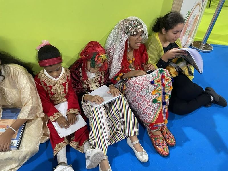 Des enfants en tenues traditionnelles colorées, assis côte à côte, plongés dans leur lecture
